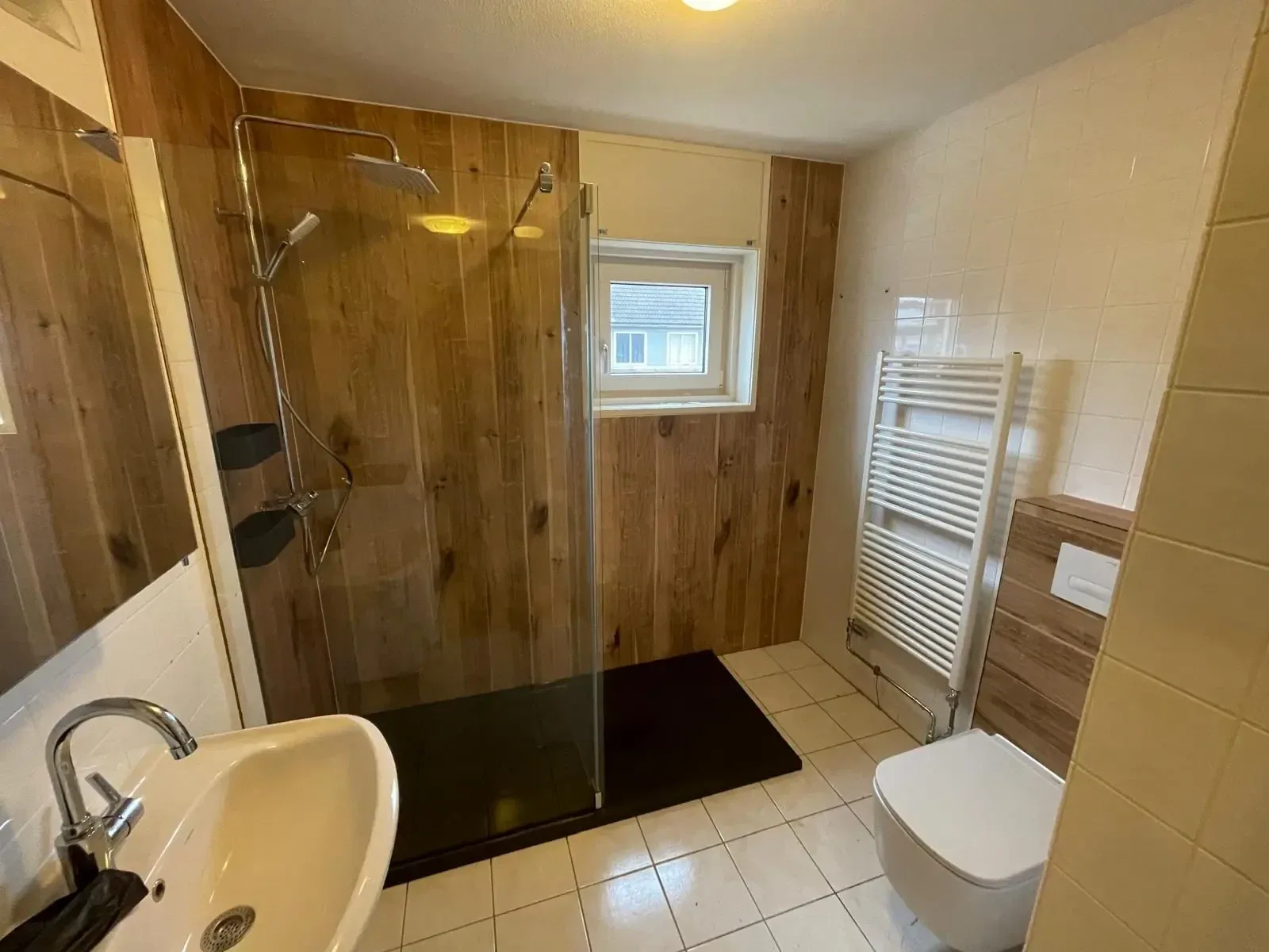 Badkamer met inloopdouche tegen houtlook wandpanelen, hangtoilet, wastafel en radiator