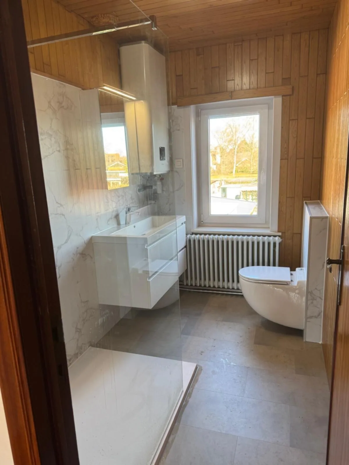 Gerenoveerde badkamer met marmerlook wandpanelen en hangtoilet