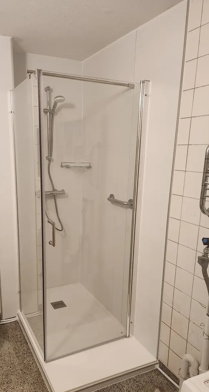 Na: Zelfde badkamer na verbouwing: ligbad vervangen door douchecabine met glazen deuren, steunbeugel en douchebak