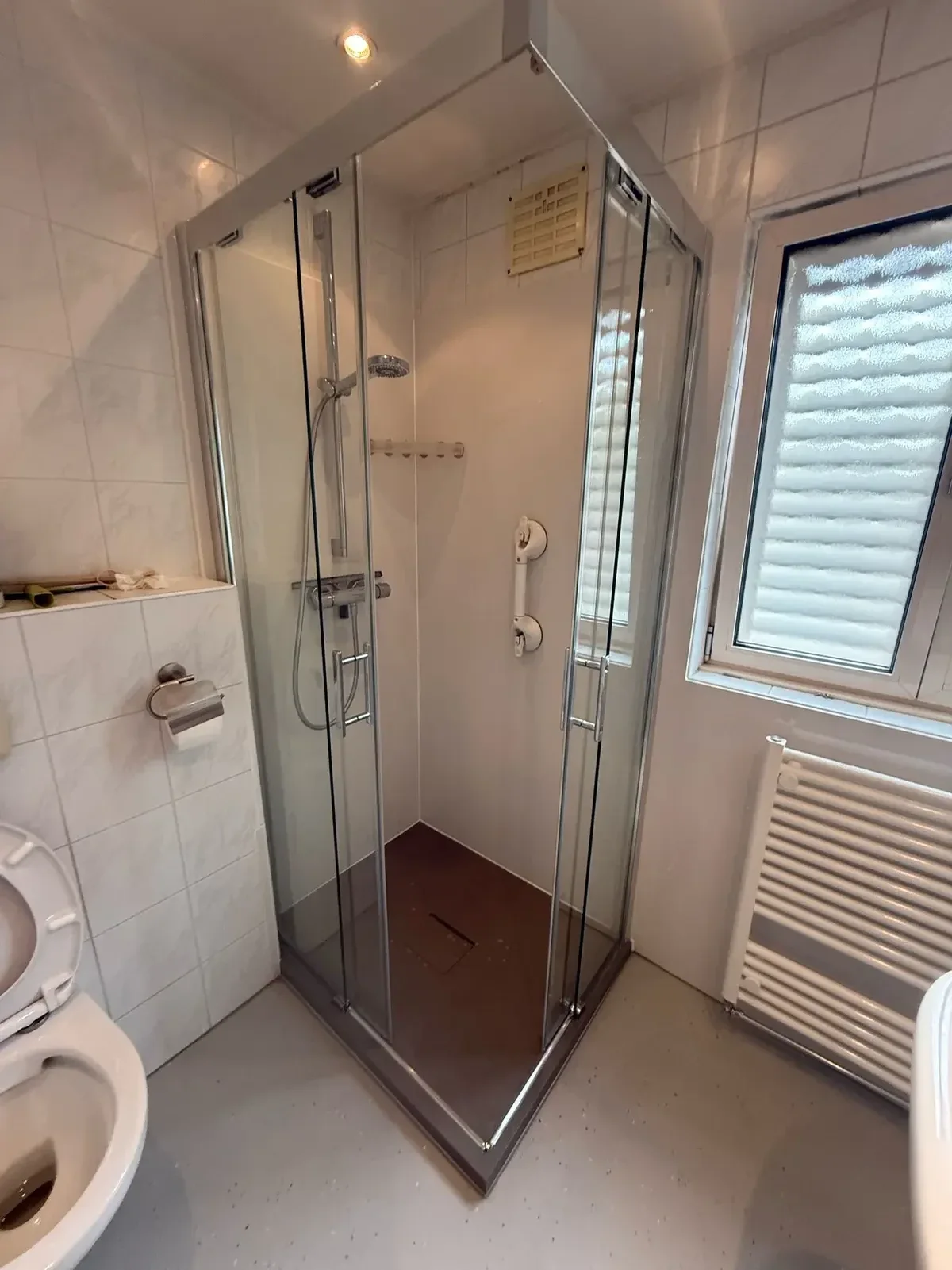 Na: Vierkante glazen douchecabine met steunbeugel, naast toilet en handdoekradiator